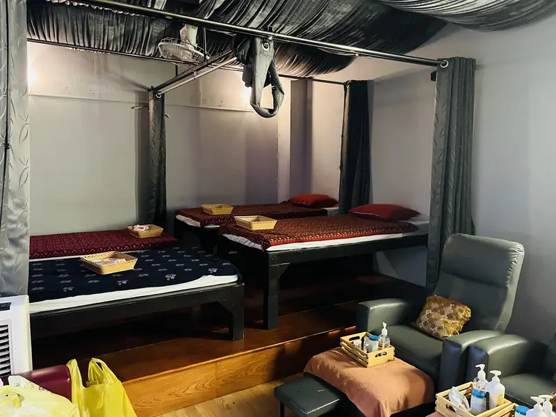Massage room with floor mattresses, red cushions and grey curtains